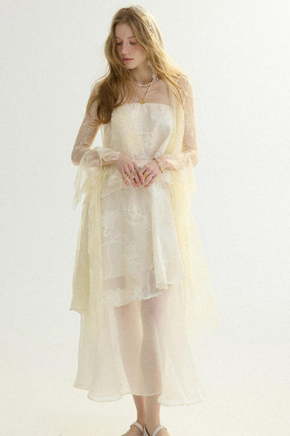 A woman modeling a cream-colored sheer lace dress with a matching long-sleeve tulle shawl, set against a plain light background.