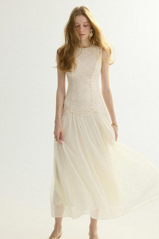 A woman modeling a sleeveless cream maxi dress with a textured lace bodice and a flowing tulle skirt, set against a plain white studio background.