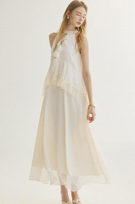 A woman modeling a sleeveless, high-neck, floor-length cream dress with layered ruffle details, set against a plain off-white studio background.
