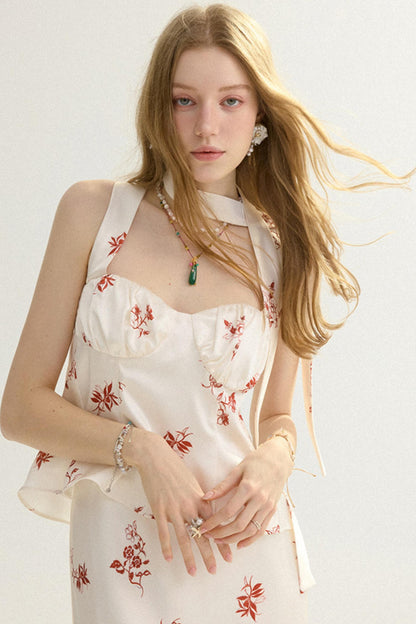 A young woman with long blonde hair wearing a cream-colored halter dress with a red floral print, styled with jewelry against a plain light background.