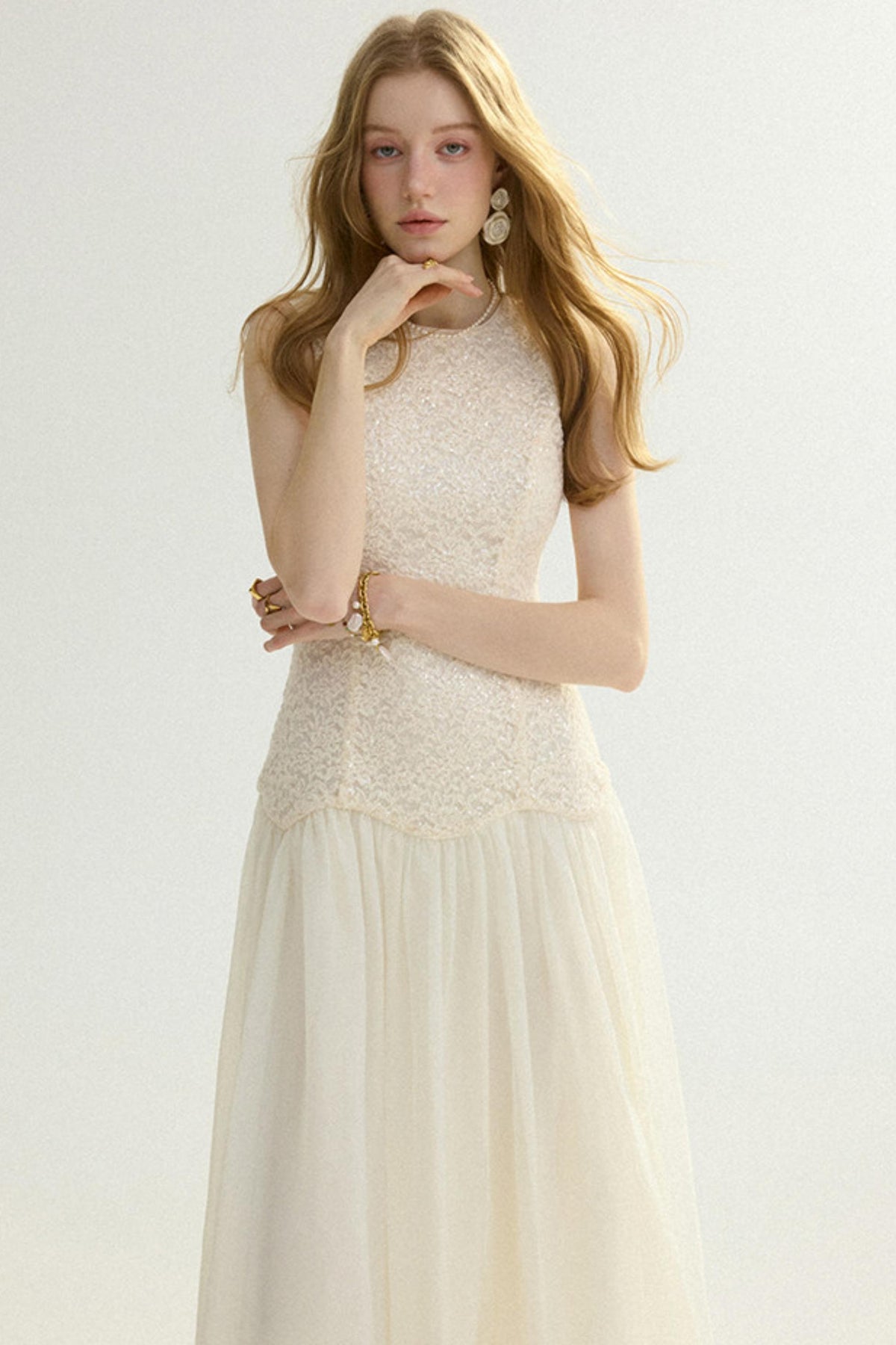 A woman modeling a sleeveless cream lace top with a matching flowing tulle skirt, photographed against a plain light background.