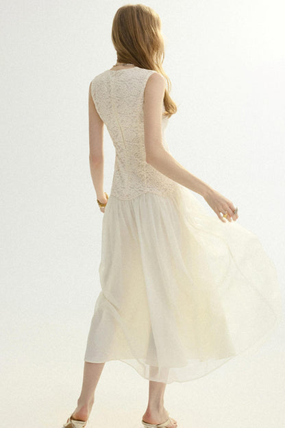 A woman shown from the back wearing a sleeveless cream-colored midi dress with a lace bodice and flowing tulle skirt, set against a plain white studio background.