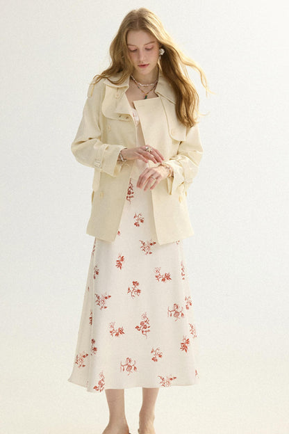 A woman modeling a cream-colored trench coat over a matching cream midi dress with a red floral pattern, set against a plain light background.