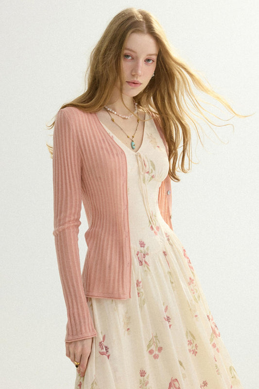 A woman wearing a light pink ribbed cardigan over a cream floral dress, photographed against a plain light background.