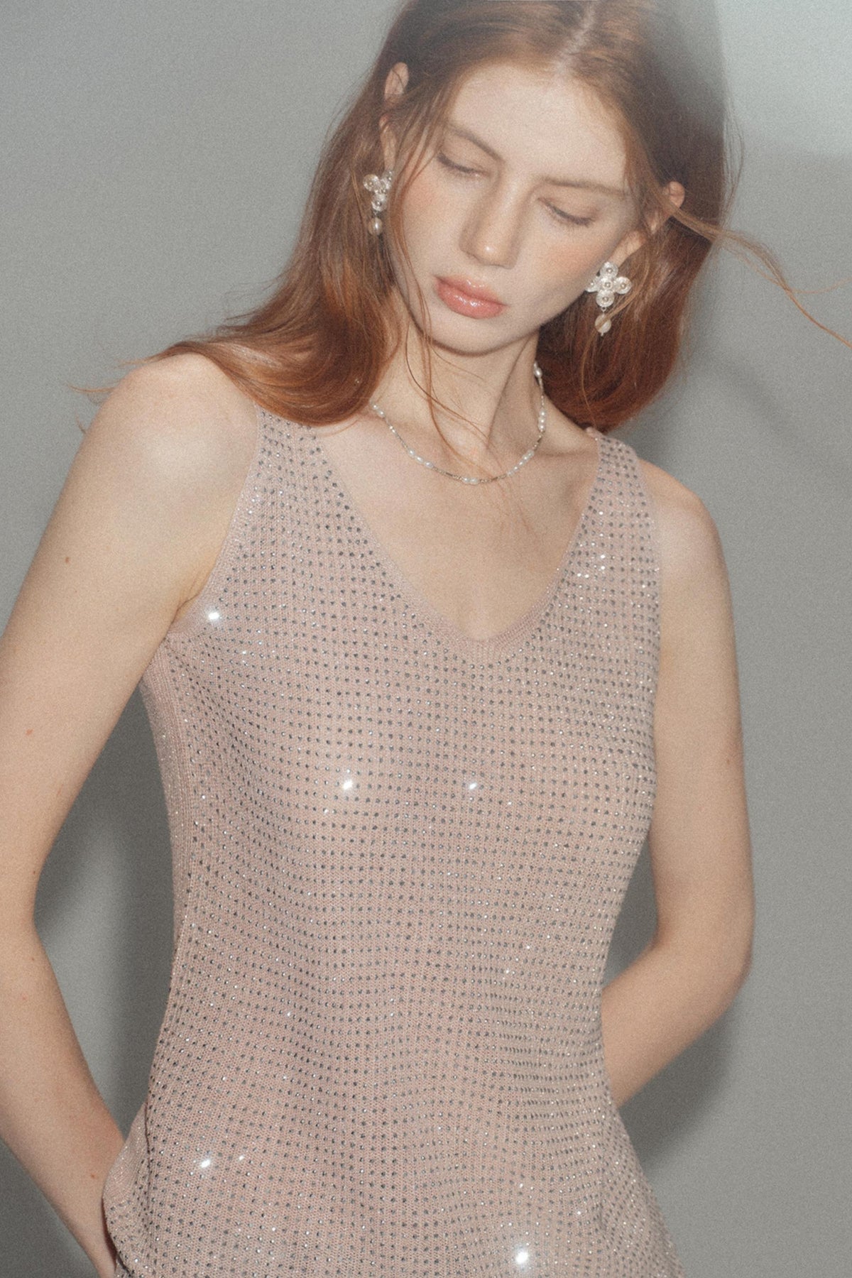 A woman wearing a sleeveless, sparkling nude-beige sequined top against a plain gray background.