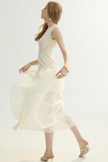 A woman wearing a sleeveless cream-colored midi dress with a textured bodice and a flowing skirt, captured in motion against a plain white studio background.
