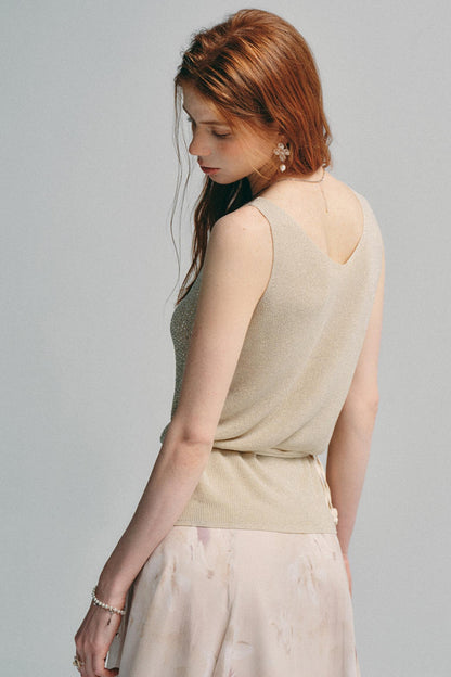 A woman with red hair is shown from the back wearing a beige sleeveless knit top and a light pink skirt against a solid gray background.