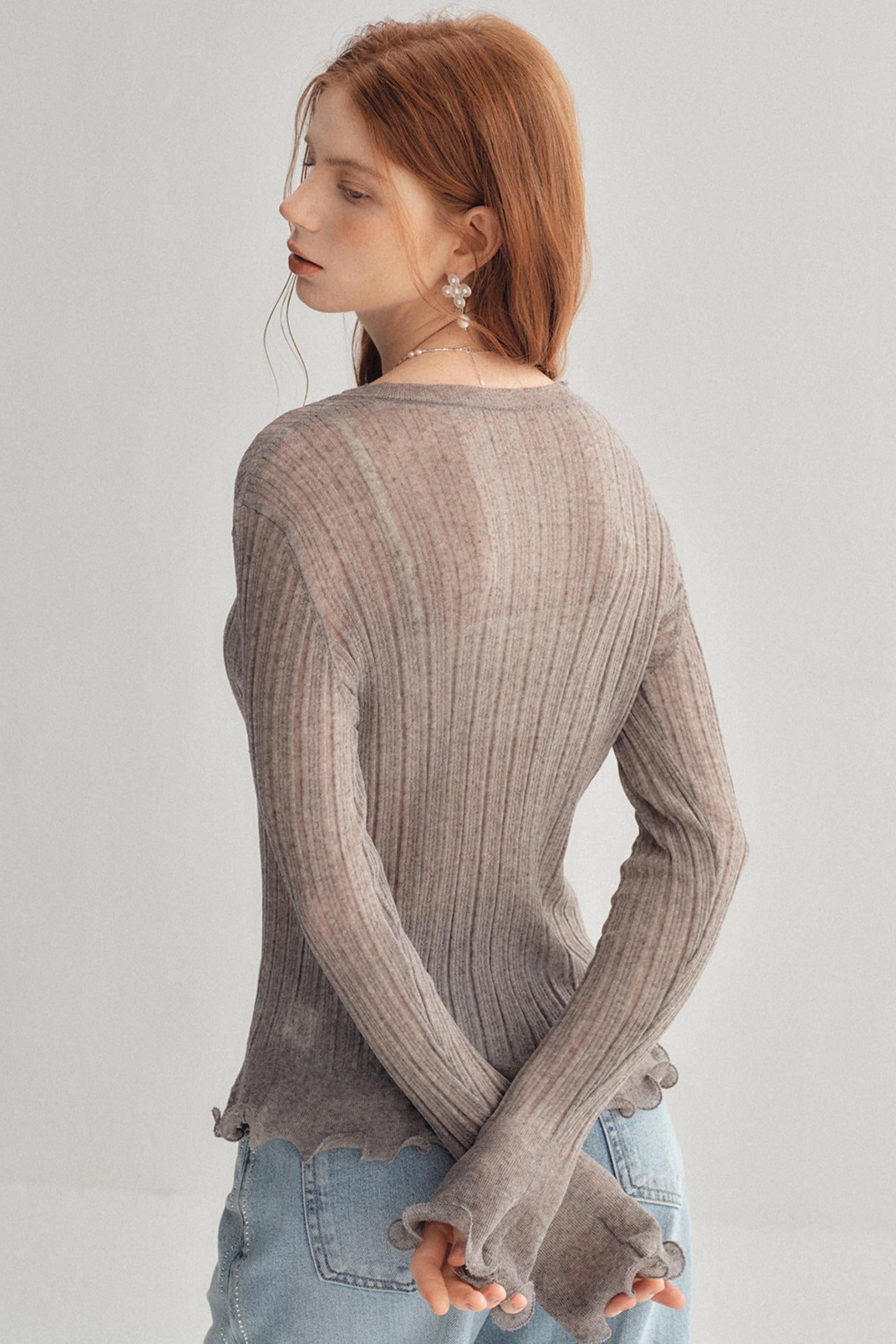 A woman with red hair is shown from the back wearing a ribbed knit long-sleeve top in a taupe-gray color, paired with light blue jeans, against a plain light gray background.