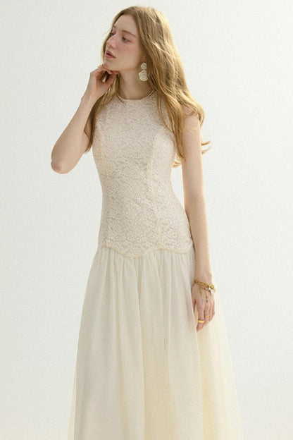 A woman modeling a sleeveless cream formal dress with a textured lace bodice and a flowing tulle skirt, set against a plain light background.