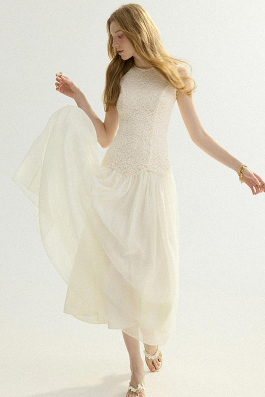 A woman modeling a sleeveless cream-colored dress with a textured lace bodice and a flowing chiffon skirt, set against a plain white studio background.
