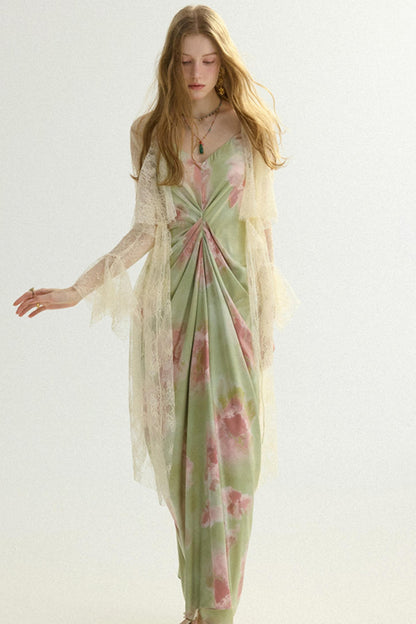 A woman modeling a long, flowing dress with a light sage green base and pink floral print, layered with a sheer cream tulle kimono-style overlay, against a plain light background.
