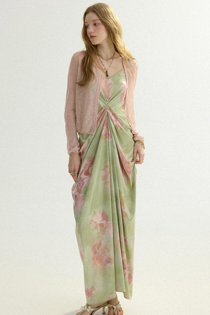 A woman modeling a long-sleeve light pink cardigan layered over a green satin slip dress with a pink floral print and a twisted waist detail, set against a plain light background.