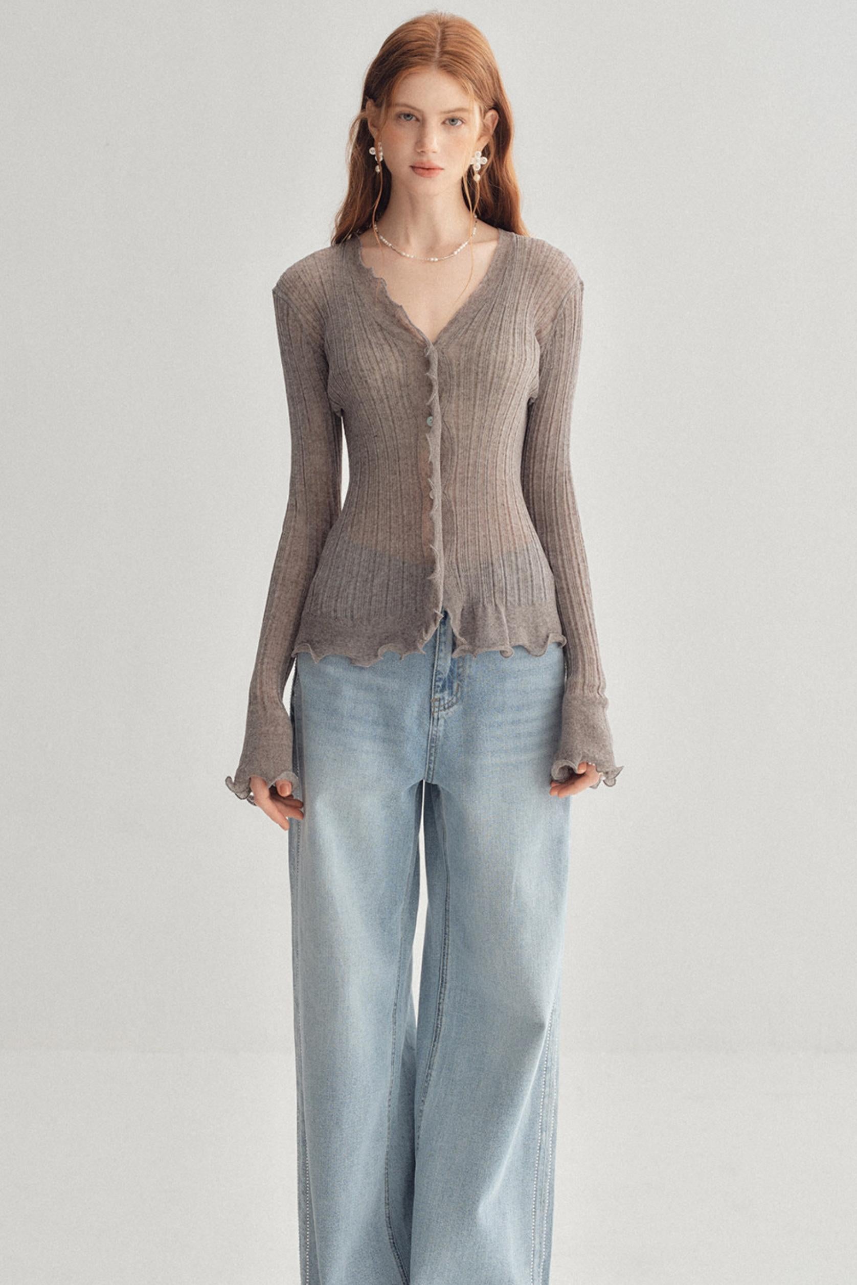 A woman modeling a taupe ribbed long-sleeve cardigan with a scalloped hem and button front, paired with light-wash wide-leg jeans, against a plain light gray studio background.