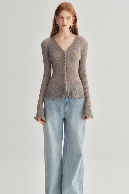 A woman modeling a taupe ribbed long-sleeve cardigan with a scalloped hem and button front, paired with light-wash wide-leg jeans, against a plain light gray studio background.