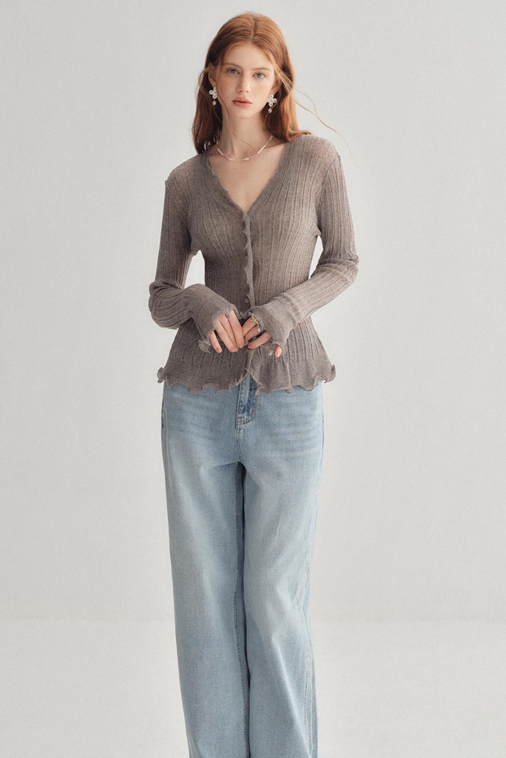 A woman modeling a taupe ribbed knit cardigan with a ruffled hem and button front, paired with light-wash wide-leg jeans, against a plain light gray studio background.