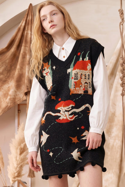 A model wearing a black knit sweater vest with whimsical embroidered illustrations of a house, a mushroom, stars, and a fox, layered over a white collared shirt. The vest features a scalloped neckline and pom-pom trim at the hem.