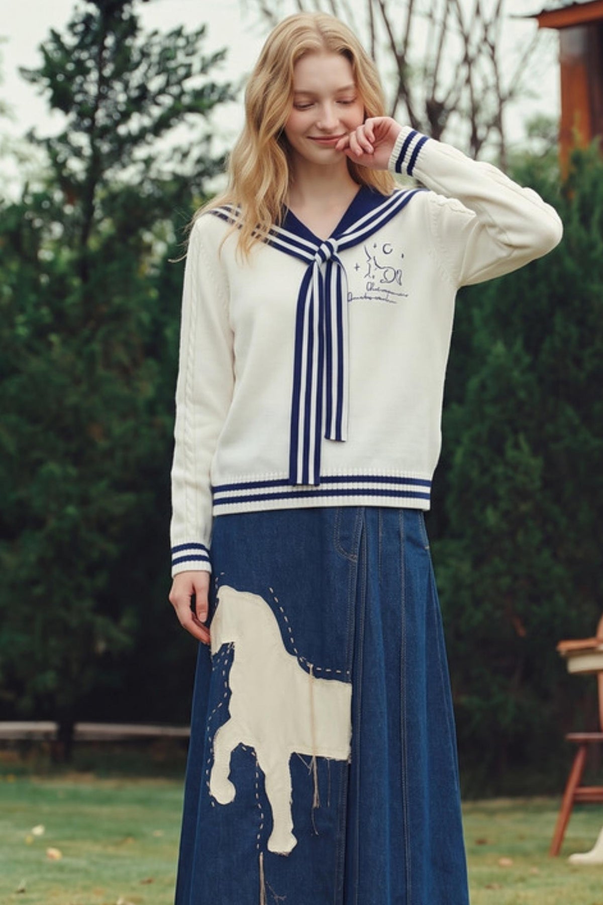 A woman stands outdoors wearing a cream knit sweater with navy blue trim and a matching navy skirt featuring a large cream patchwork motif.