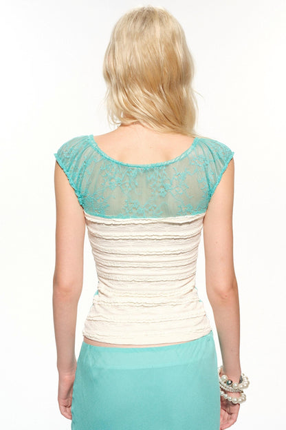 A woman shown from the back wearing a short-sleeve top with a turquoise lace upper back and cap sleeves, and a cream ruched body, paired with a turquoise skirt against a white studio background.