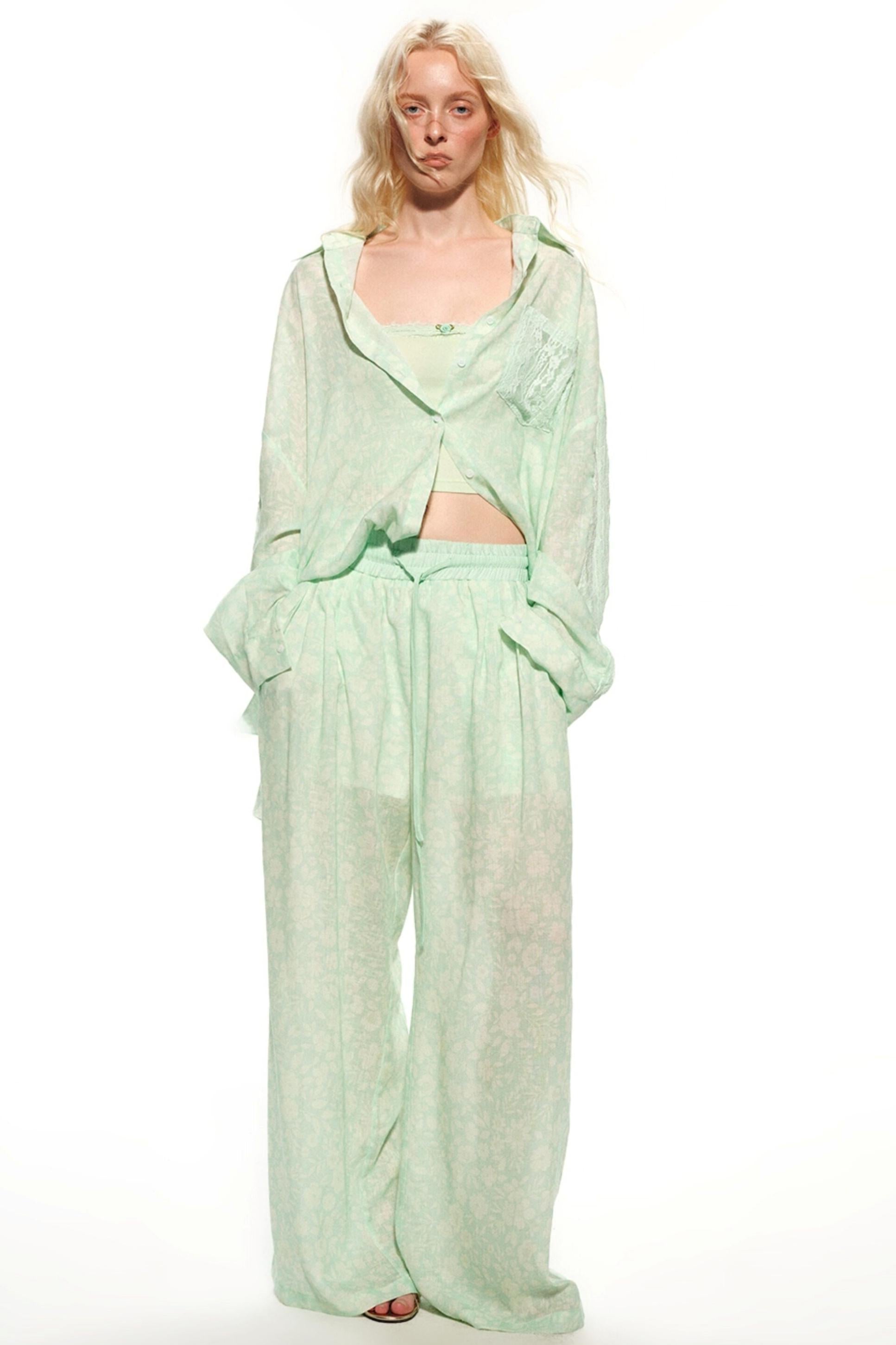 A model wearing a light mint green two-piece outfit consisting of a long-sleeve cropped top and matching wide-leg pants, photographed against a solid white studio background.
