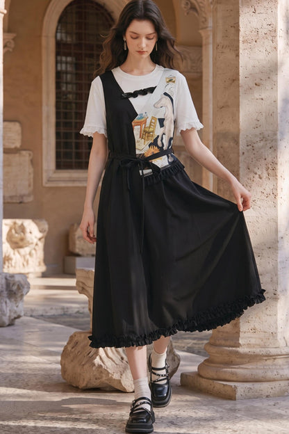 A woman models a black midi skirt with a ruffled hem and a matching black waist tie over a white graphic t-shirt, standing in a stone courtyard.