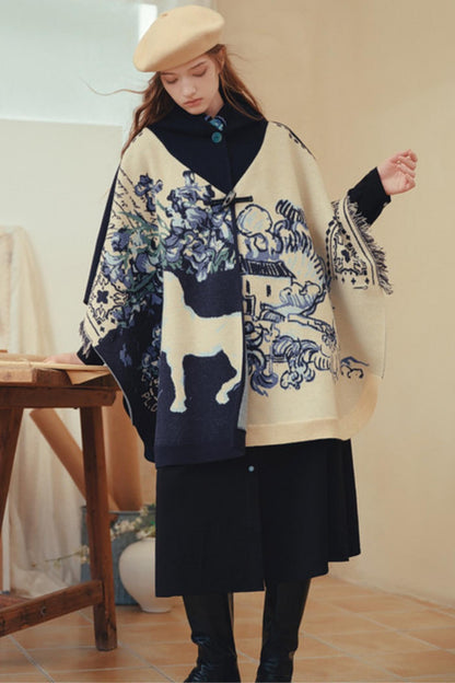 A woman wearing a cream and navy blue patterned poncho over a black dress, black boots, and a beige beret, standing in a softly lit indoor setting.