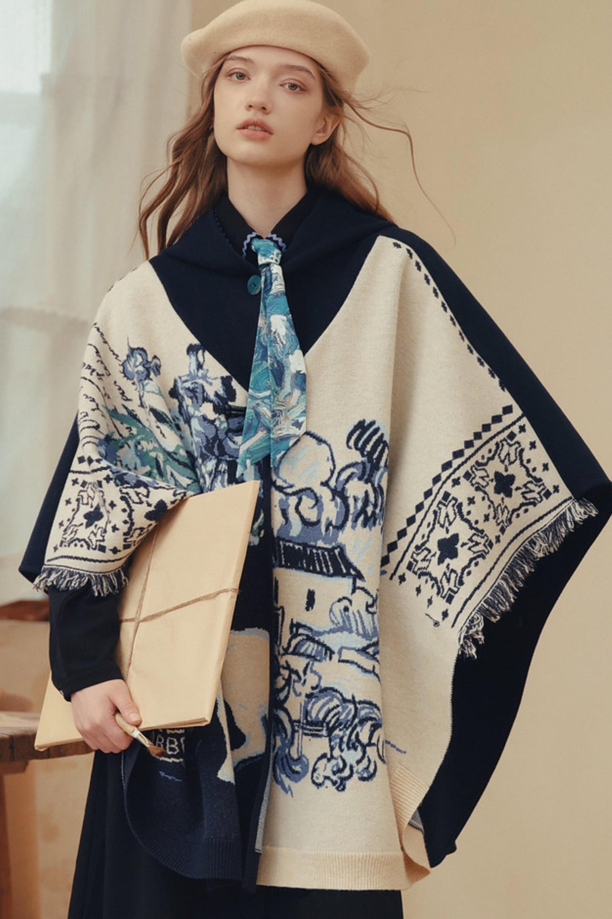A woman wearing a beige beret and holding a beige clutch bag, wearing a cream and navy blue patterned shawl over a dark dress.