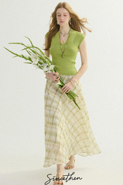 Woman wearing a green top and plaid skirt holding flowers on a white background