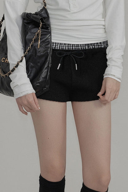 Person wearing a white long-sleeve shirt, black shorts, and black knee-high socks with a plain background.