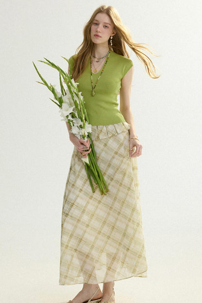 Woman wearing a green top and plaid skirt holding flowers against a white background