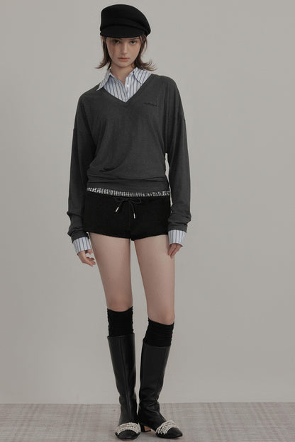 Person wearing a dark sweater, black shorts, knee-high boots, and a cap on a plain background