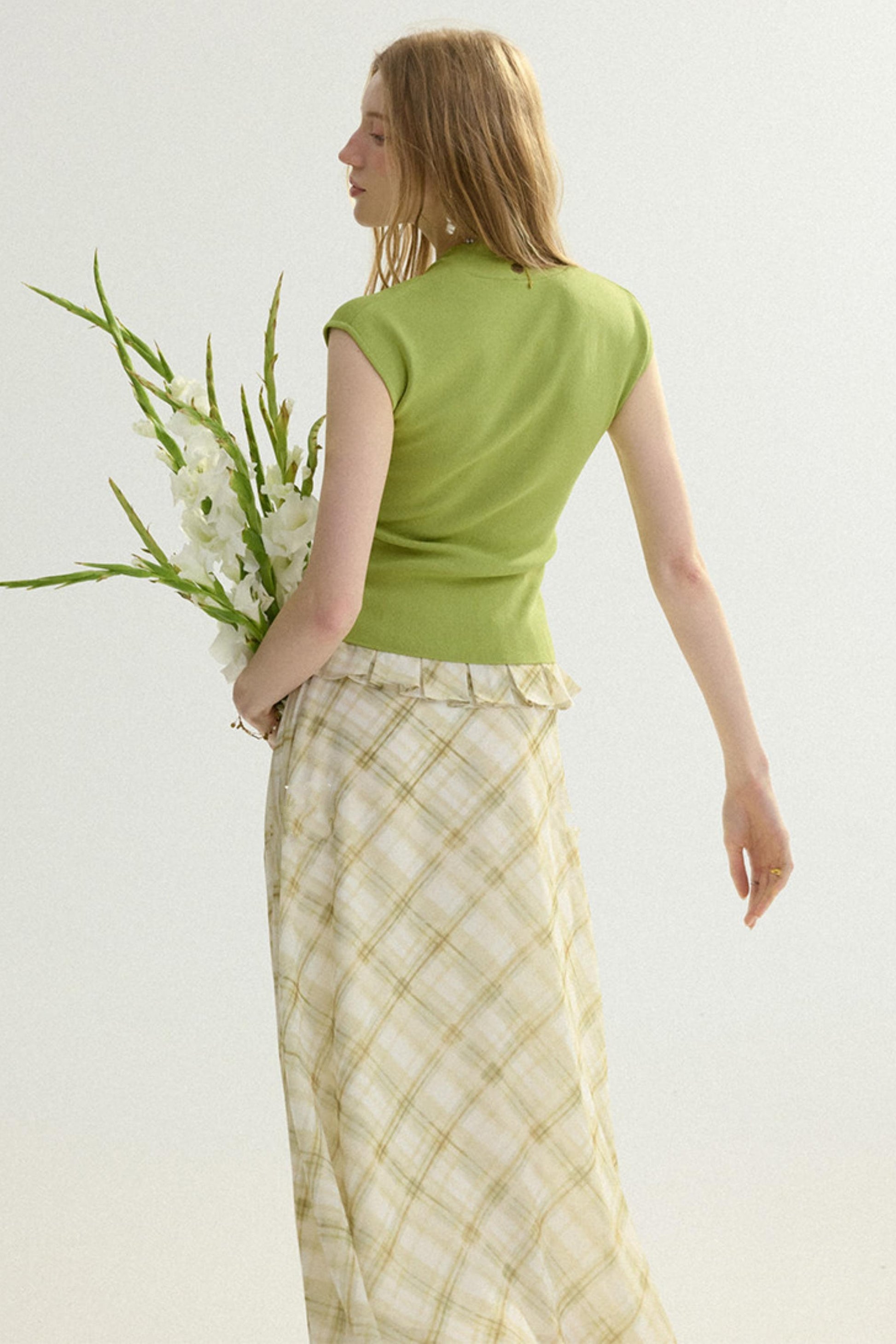 Woman in a green top and checkered skirt holding flowers against a white background