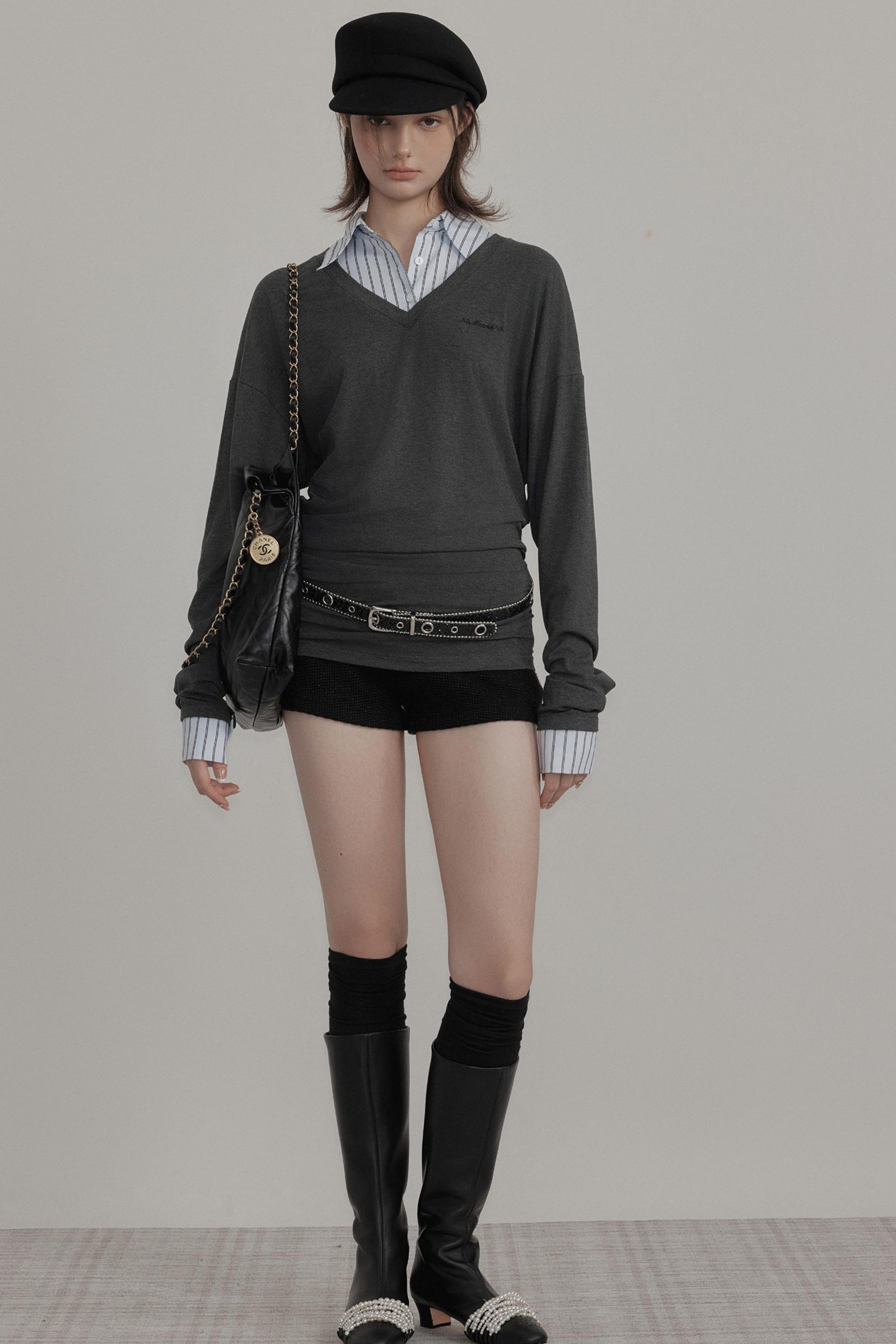 Person wearing a dark sweater, shorts, and boots on a plain background