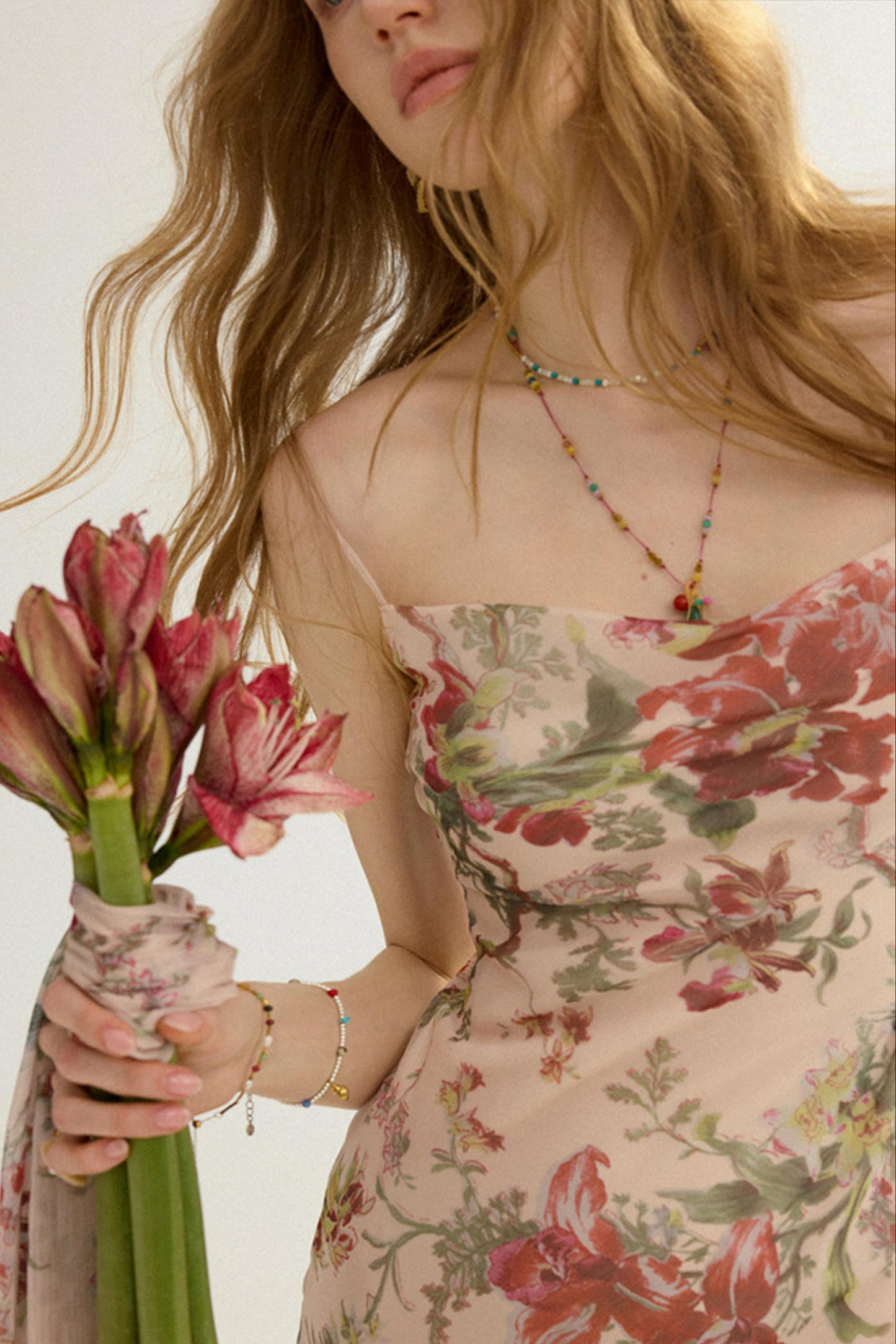 Woman holding pink flowers wearing a floral dress with a neutral background