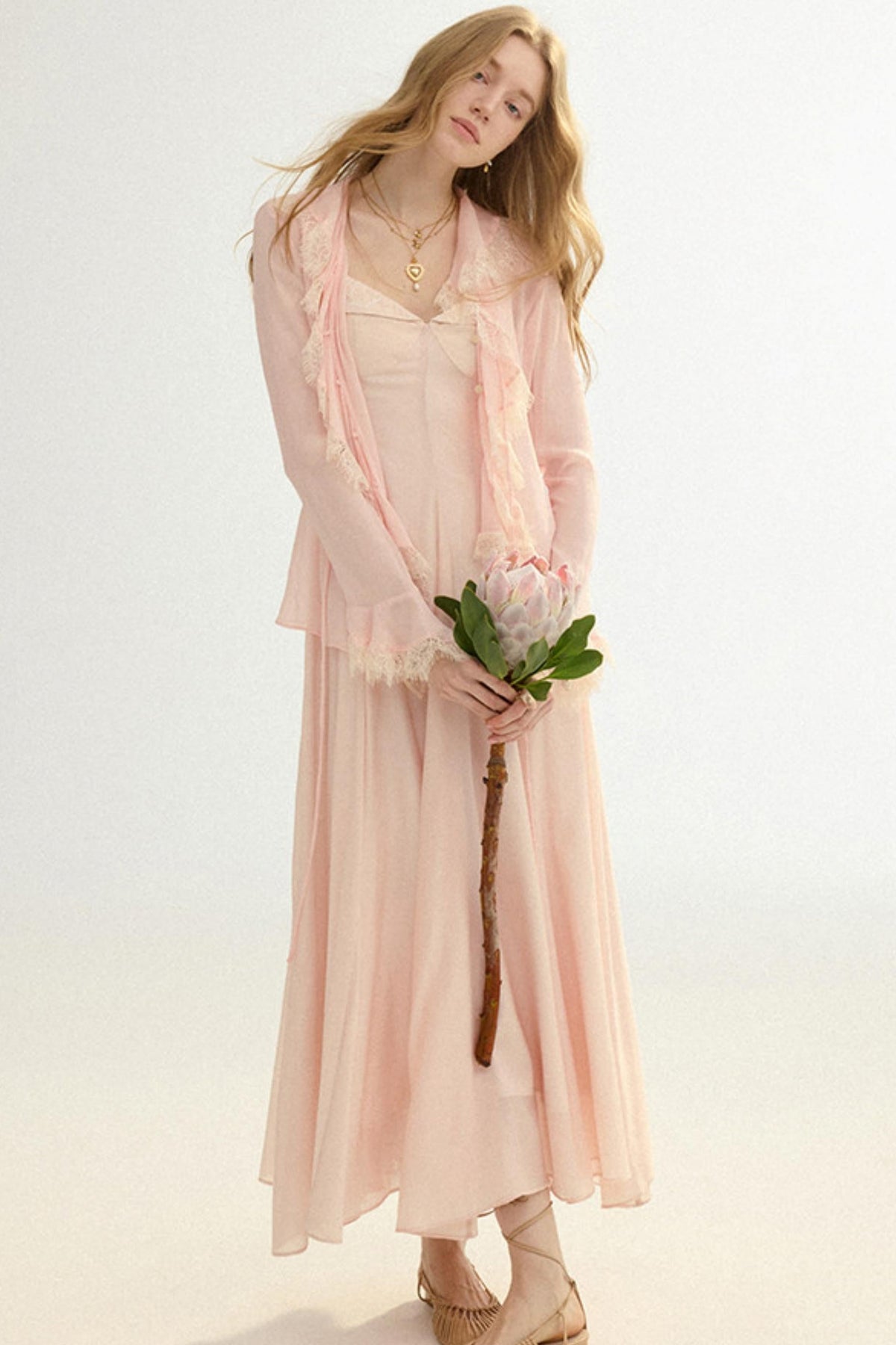 Woman in a light pink dress holding a flower against a white background