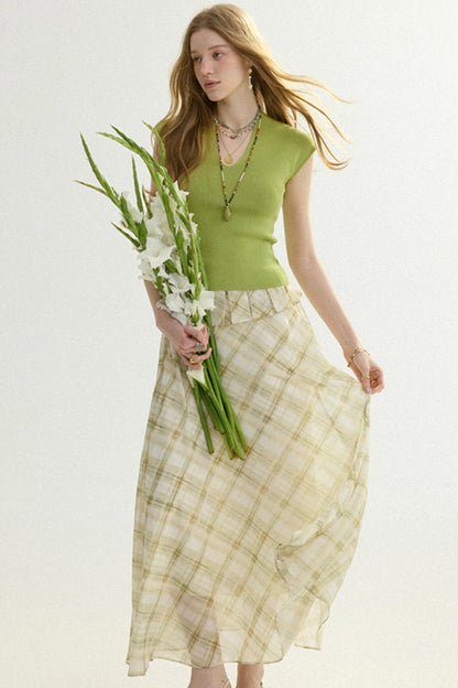 Woman holding flowers wearing a green top and plaid skirt on a light background
