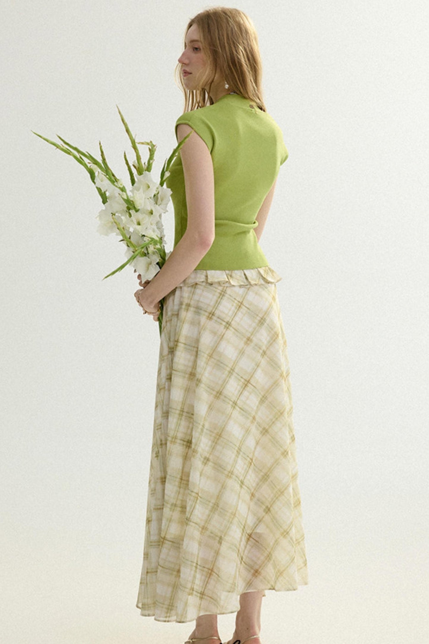 Woman wearing a green top and plaid skirt holding flowers on a white background