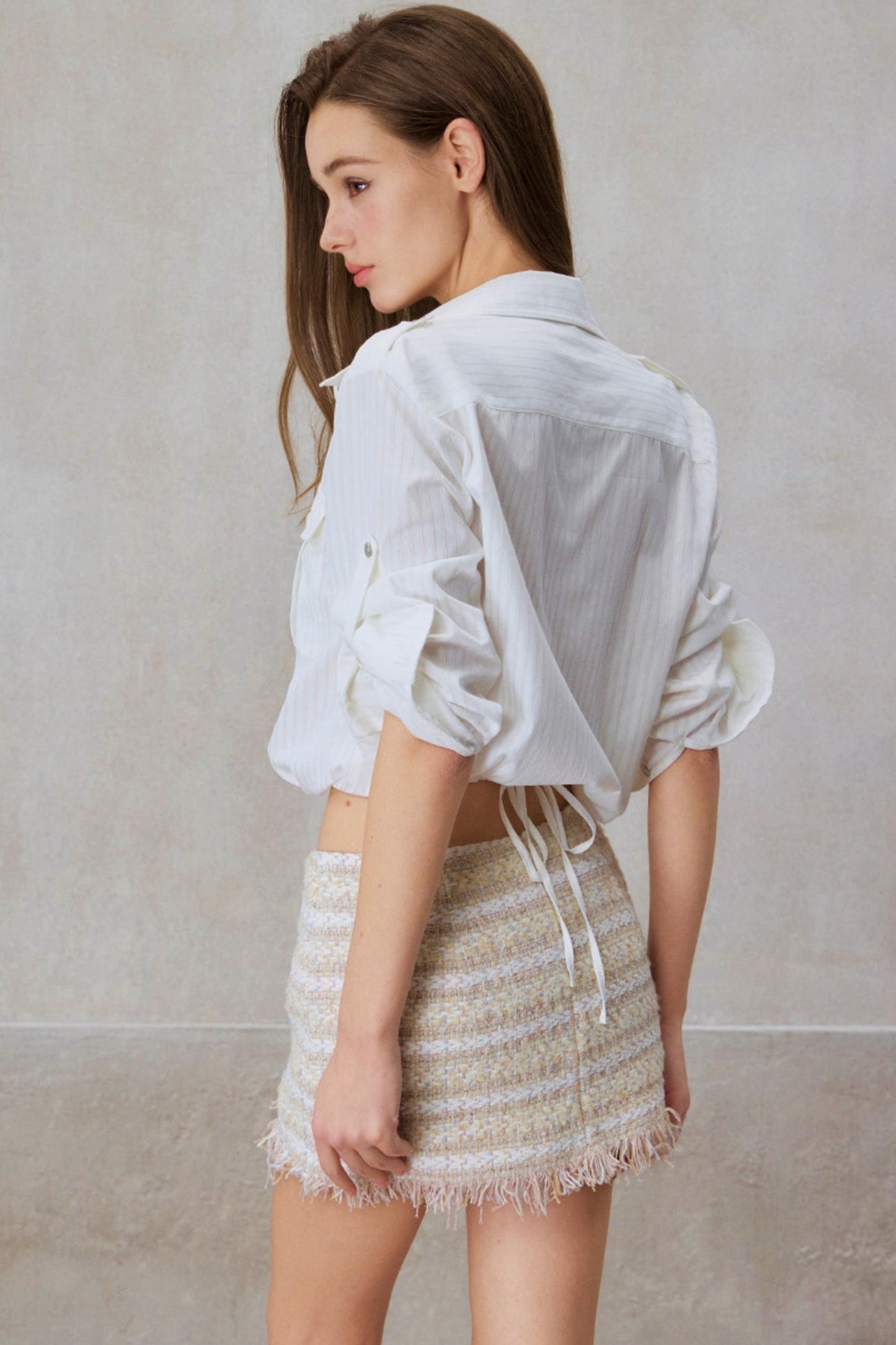 Woman wearing a white blouse and beige skirt against a plain background