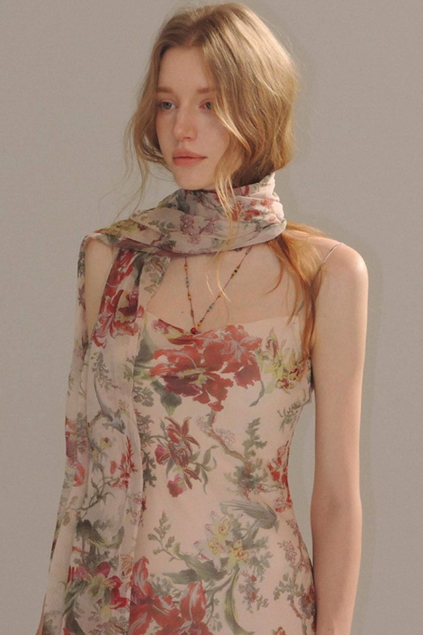 Woman wearing a floral dress with a matching scarf against a plain background