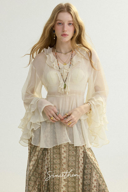 Woman wearing a sheer blouse with ruffles and a patterned skirt on a white background