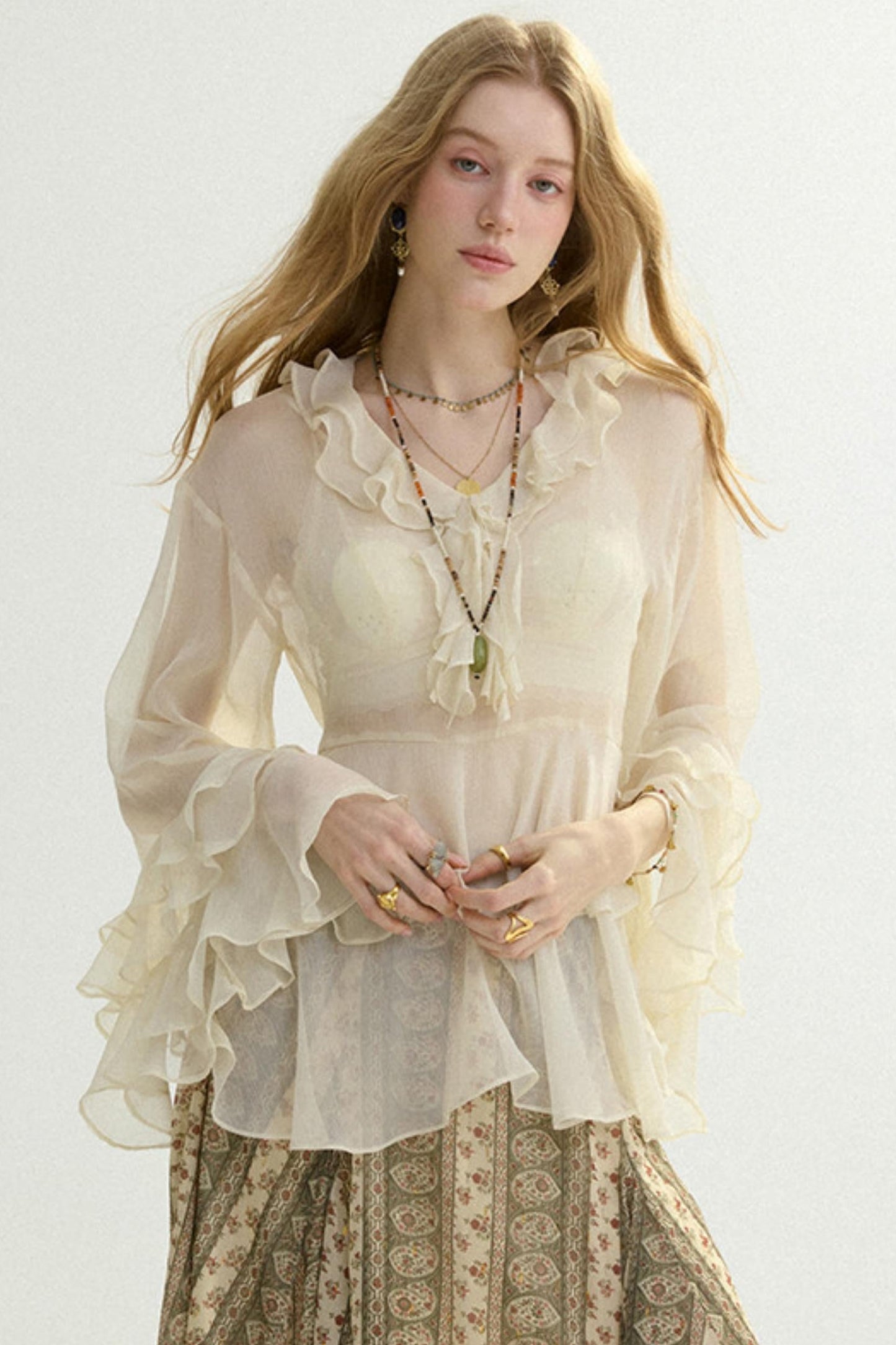 Woman wearing a light blouse with ruffled sleeves and a patterned skirt on a white background