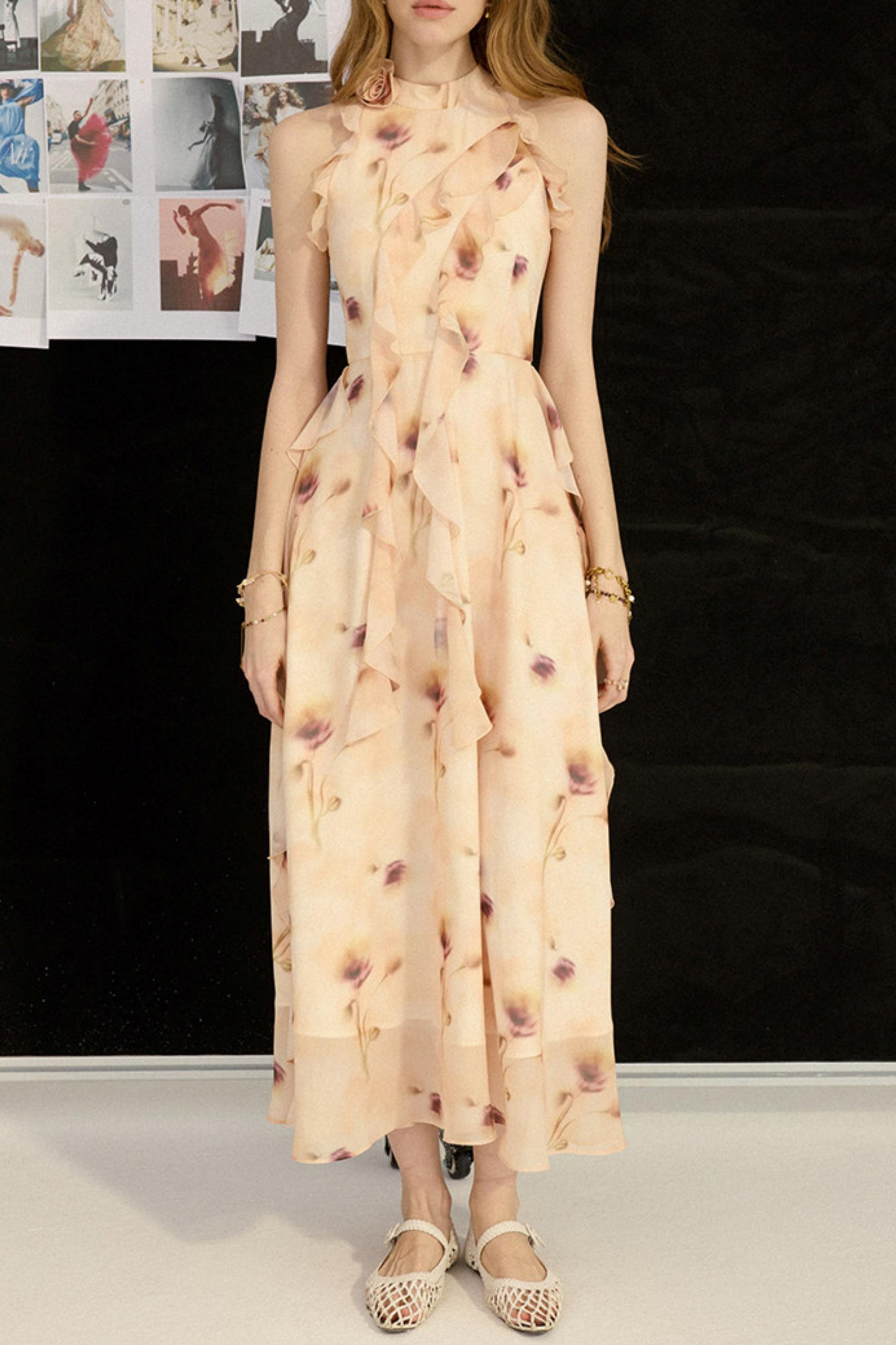 Woman wearing a long, patterned dress in a room with a black wall and posters.