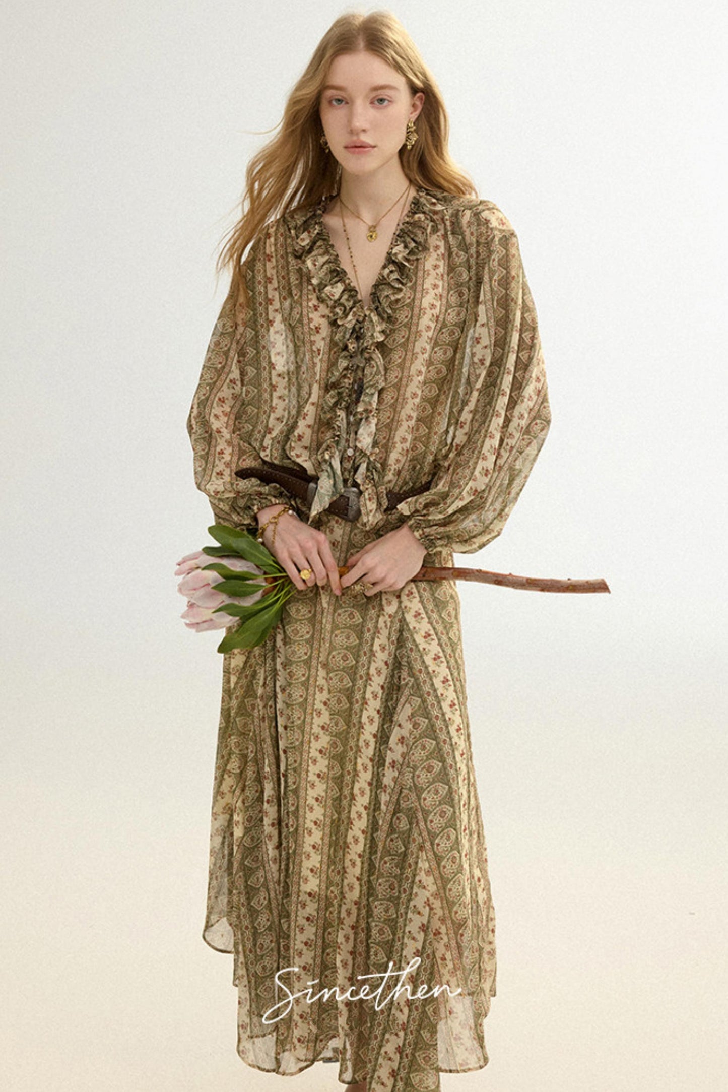 Woman wearing a patterned dress holding flowers against a plain background