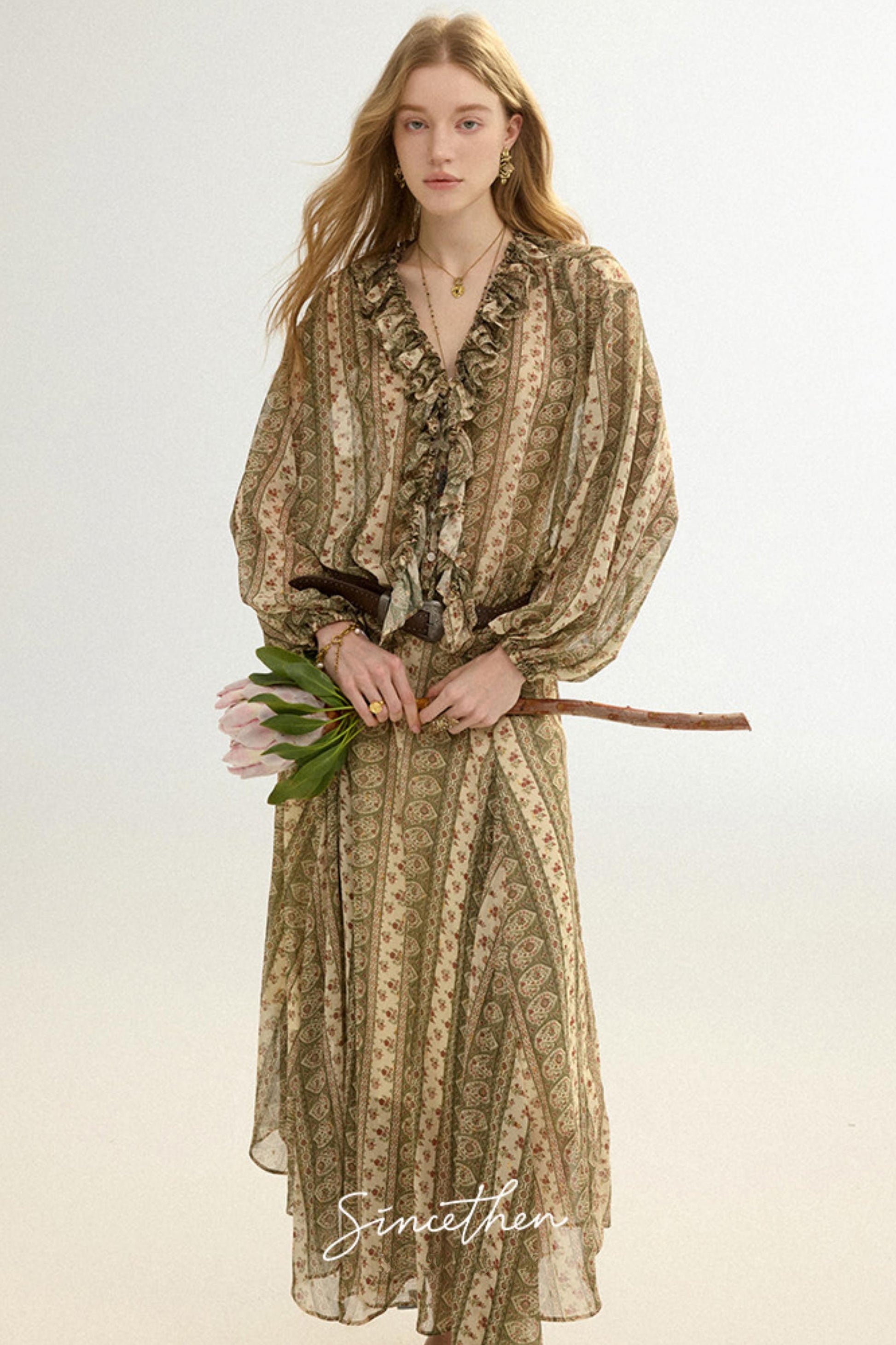 Woman wearing a patterned dress holding flowers against a plain background