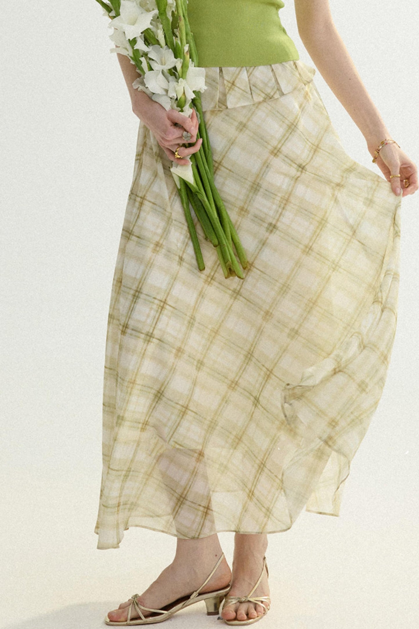 Person wearing a long checkered skirt holding flowers on a plain background