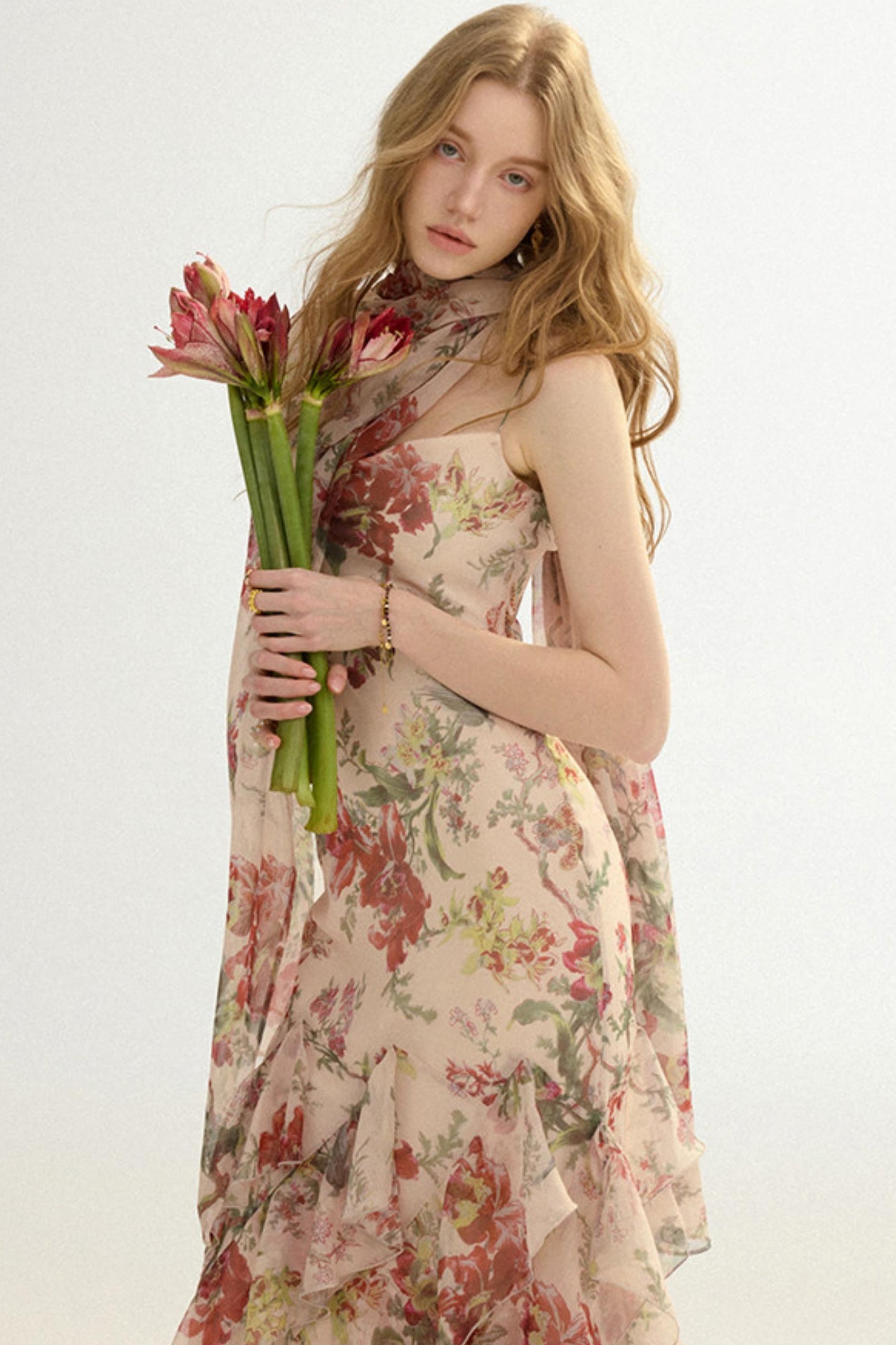 Woman in a floral dress holding flowers against a plain background