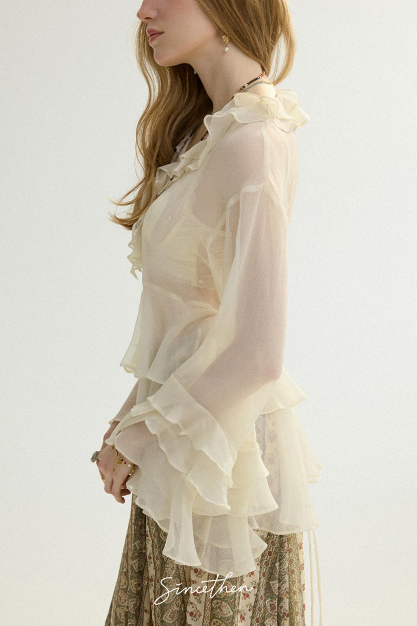 Woman wearing a light-colored blouse with ruffled details on a plain background