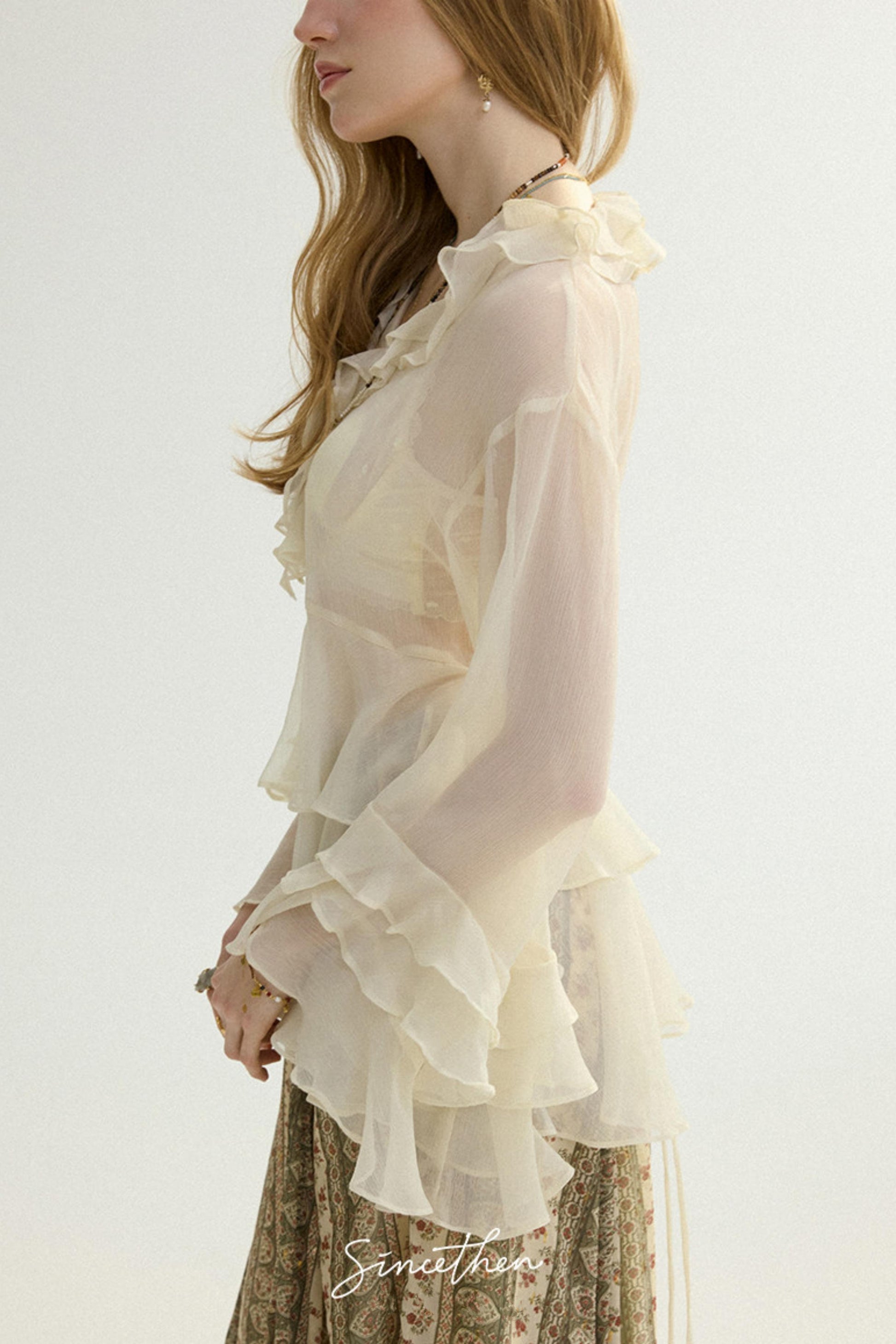 Woman wearing a light-colored blouse with ruffled details on a plain background
