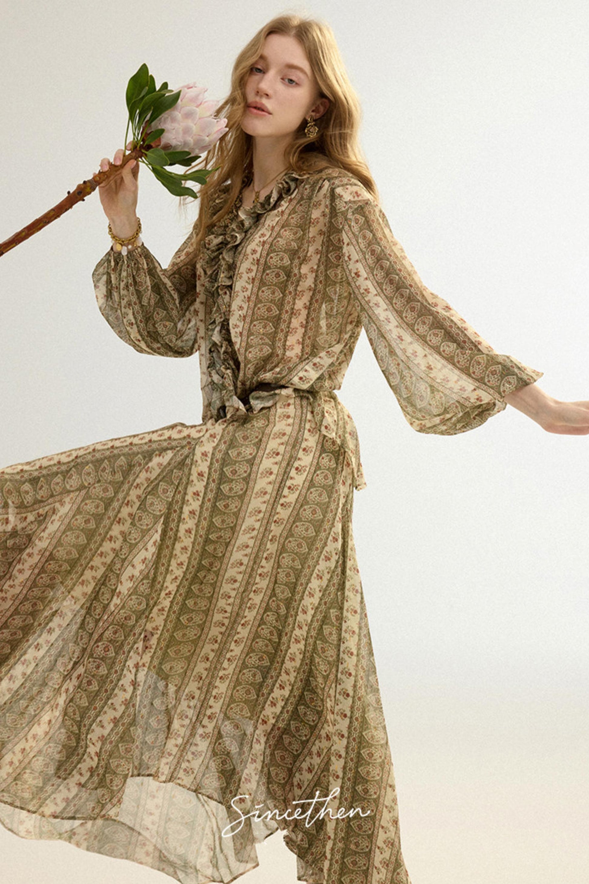 Woman wearing a long, patterned dress holding flowers against a light background