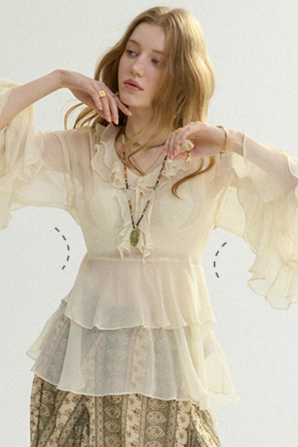 Woman wearing a light-colored blouse with sheer sleeves against a white background