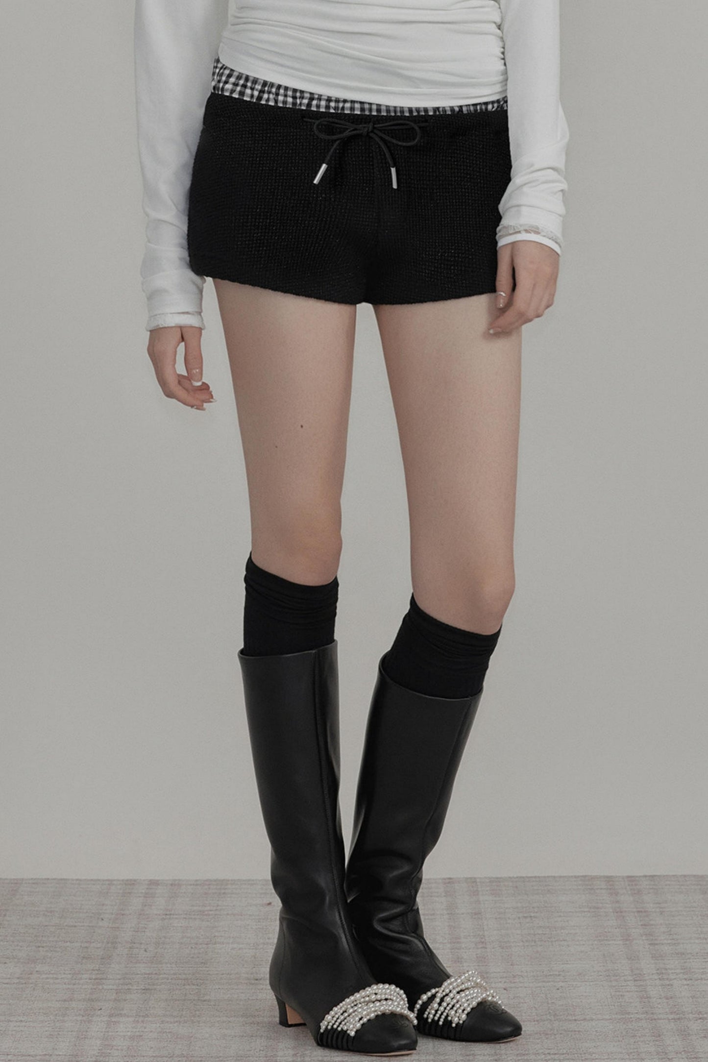 Person wearing black knee-high boots with a plain background